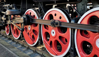 Old steam engine locomotive wheels and other parts, close-up view. Black and red iron details of vintage train. Industrial retro background.