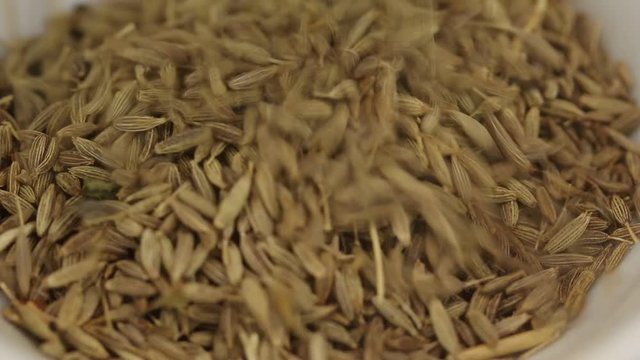 Zira seeds fall in a glass transparent bowl, close-up
