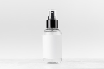 Transparent spray bottle for cosmetics product with white blank label on white wood board, mock up...