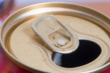 An opened aluminum can with some drink on can opener.