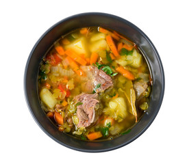 Meat soup with vegetables in black bowl isolated on white. Top view