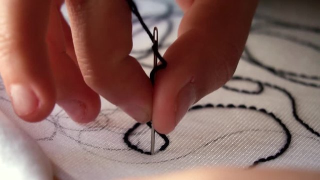 Dedos empujando aguja sobre tela blanca