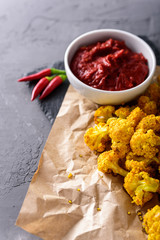 vertical image of cauliflower in batter on craft paper with chili sauce on dark background