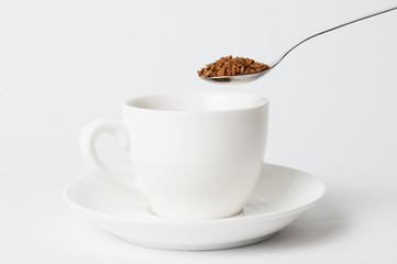 Instant coffee spoon over white cup on white background