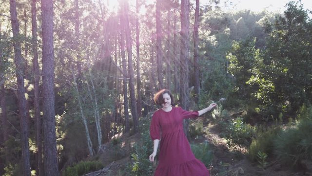 Young woman in red dress perform slow motinon spin in forest at sunset
