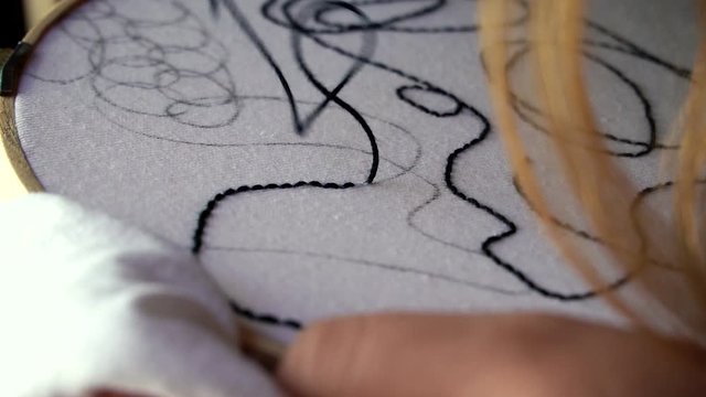 Mano femenina bordando textura abstracta sobre tela blanca