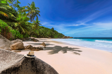 Tropical beach with beautiful rocks and straw hat under coconut palm trees and turquoise sea in Paradise island on Seychelles. 