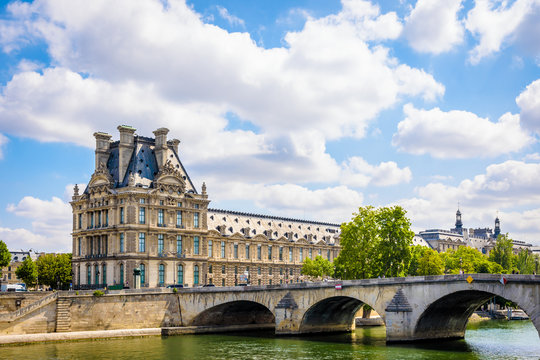 The Pavillon de Flore at the end of the Denon wing of the Louvre palace in Paris, France, with the pont Royal over the river Seine in the foreground by a sunny summer day.