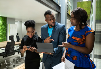 Three black african colleagues walking through coworking workspace strategizing on their way to...