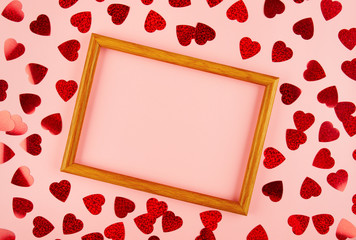 Flat lay view at wooden frame among heart shaped tinsel on pink background