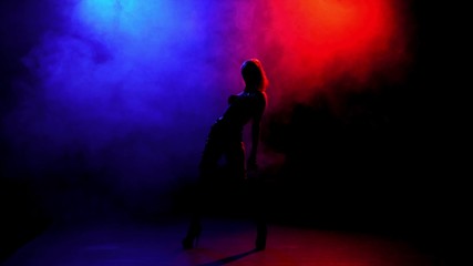 Fototapeta na wymiar Silhouetted girl dancing in the dark on a background of smoke smoke red and blue