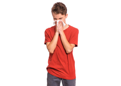 Portrait Of Unhealthy Sick Teen Boy With Napkin Close His Nose From Allergy Or Rhinitis. Unhappy Ill Child Suffering From Running Nose And Sneezing And Blow His Nose Isolated On White Background.