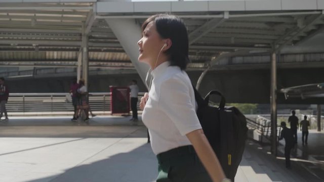Portrait of asian woman with earphone listening music using smartphone for chatting or browsing and walking up stairs in the city. Technology in everyday life and travel.