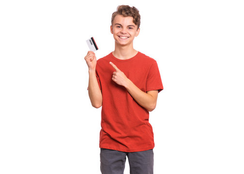 Portrait Of Happy Teen Boy With Credit Card, Isolated White Background. Smiling Child Pointing Finger On Card. Teenager Showing Credit Or Debit Card Having Fun.