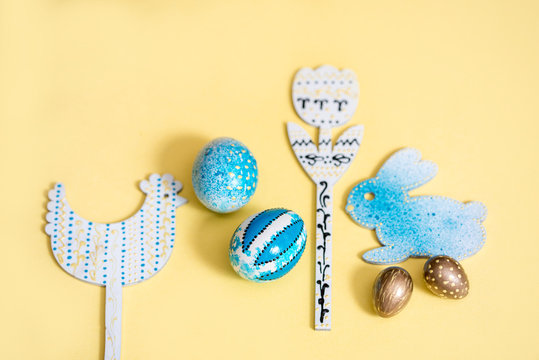 Candy color easter Blue and Gold Quail Eggs. Wooden painted chicken, hare and flower on a yellow background. gray napkin.