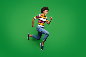 Fototapeta na wymiar Full body profile side photo of crazy cheerful afro american girl jump run after fall discounts feel rejoice emotions wear bright clothing blue sneakers isolated over green color background