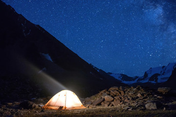 Fototapeta na wymiar Starry night mountain landscape with glowing tent.