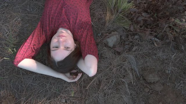 Top view of young woman in red dress lays on the ground in forest during sunset