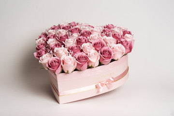 Flowers in bloom: A large bouquet of pink and white roses in a box in the shape of a heart on a white background.