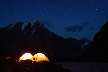 Fototapeta na wymiar Starry night mountain landscape with glowing tents.