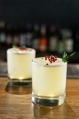 Green lime cocktail with white foam served in rocks glass on the wooden bar table decorated with red dried pepper and rosemary