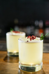 Green lime cocktail with white foam served in rocks glass on the wooden bar table decorated with red dried pepper and rosemary