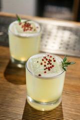 Green lime cocktail with white foam served in rocks glass on the wooden bar table decorated with red dried pepper and rosemary