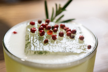 Green lime cocktail with white foam served in rocks glass on the wooden bar table decorated with red dried pepper and rosemary
