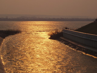View from the embankment of the confluence of one river to another in the orange-Golden-red rays of the setting sun