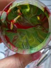 A woman's hand holds a jar of mixed paint with green, red and white stains