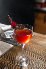 Red cocktail in the wine glass decorated with dried slice of lime and cherry served on the wooden bar desk