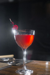 Red cocktail in the wine glass decorated with dried slice of lime and cherry served on the wooden bar desk