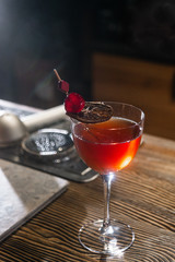 Red cocktail in the wine glass decorated with dried slice of lime and cherry served on the wooden bar desk