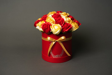 Flowers in bloom: A bouquet of red and golden roses in a red round box on a gray background.
