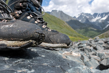 Fototapeta na wymiar Old worn out trekking boots on the background of alpine landscape.