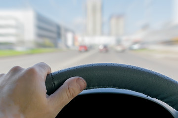 the driver's hand on the steering wheel of a car that passes on the highway against the background...