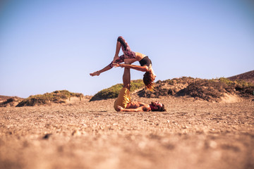 couple of two adults doing acroyoga together at the beach on the sand - man holding his teammate with his legs