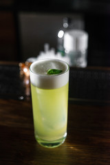 Green cocktail on bar counter. Drink with martini, gin, rum, tequila with alcohol and white foam on...