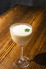 Yellow matte cocktail in the wine glass with foam served on the wooden bar table decorated with green leaf on the top 