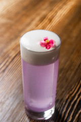 Space violet alcoholic drink in the big cocktail glass decorated with a red flower on the wooden bar desk counter under the studio lights