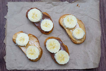 Sandwiches with peanut butter and chocolate paste with banana slices on a dark background. Home Fast Food Concept
