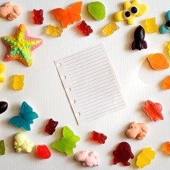 Multicolor jelly candy frame with blank sheet of paper on white wood background. Happy sweet childhood concept. Top view with copy space for your text
