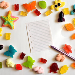Multicolor jelly candy frame with blank sheet of paper on white wood background. Happy sweet childhood concept. Top view with copy space for your text