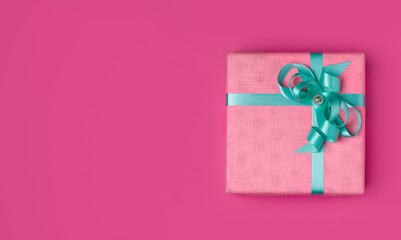 Pink gift with a turquoise ribbon on a pink background with place for copy space. The concept of the holiday of March 8, Valentine's day or birthday.