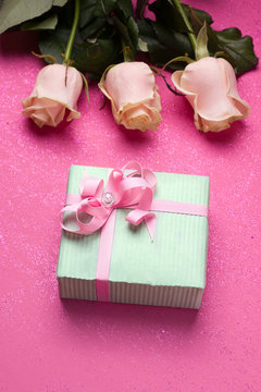 gift in mint packing on a pink background with flowers. Vertical image. The concept of a birthday holiday, women's day.