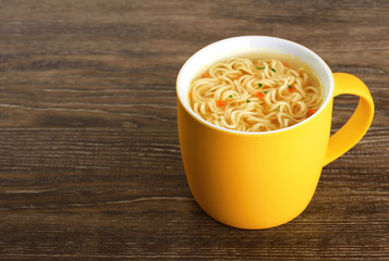 Hot cup of instant chicken noodle soup on wooden background.