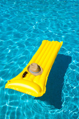 Hat and sunglasses resting on bright yellow inflatable raft floating in blue swimming pool