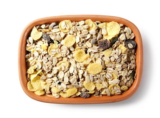 Muesli mixture of wholegrain foods, cereals, seeds and raisins in clay bowl isolated on white background, top view