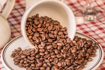 Roasted coffee beans in cup and plate on coffeeshop table. Fresh gourmet flavor aroma. Delicious fair trade cafe cappuccino or espresso ingredient. The bean bunch was fallen over at breakfast