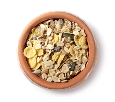 Muesli mixture of wholegrain foods, cereals, seeds and raisins in clay bowl isolated on white background, top view